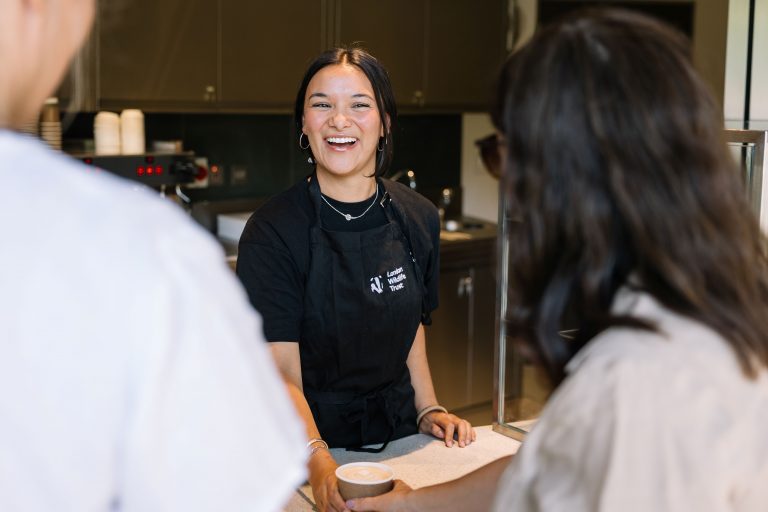 A smiling woman serving coffee at the cafe kiosk.